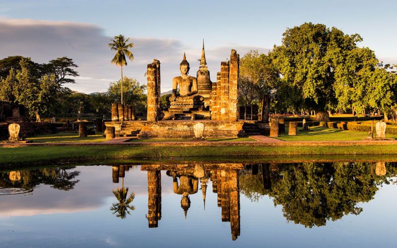 Ancient temple ruins in Sukhothai Historical Park, Thailand, reflected in a tranquil pond at sunset