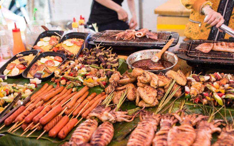 Vietnamese street food stall with grilled seafood, skewered meats, sausages, and vegetables prepared over charcoal grills.