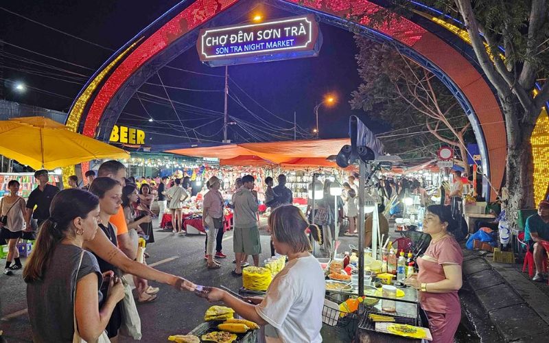 Bustling evening scene at Son Tra Night Market in Da Nang, Vietnam, where visitors explore street food stalls and local souvenirs under vibrant lights