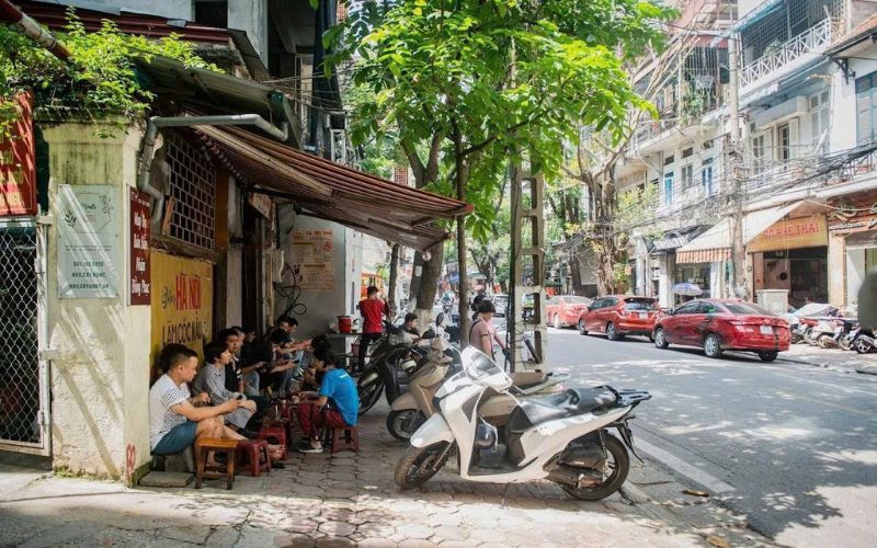 Locals relaxing at a sidewalk café on Triệu Việt Vương Street, a famous coffee hub in Hanoi lined with vintage buildings and shady trees