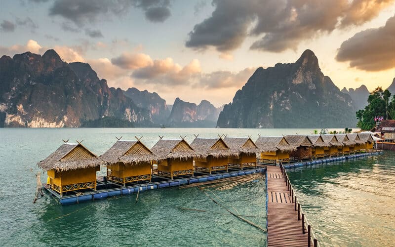 Floating bungalows on Cheow Lan Lake in Khao Sok National Park at sunset, surrounded by towering limestone cliffs and calm emerald waters.