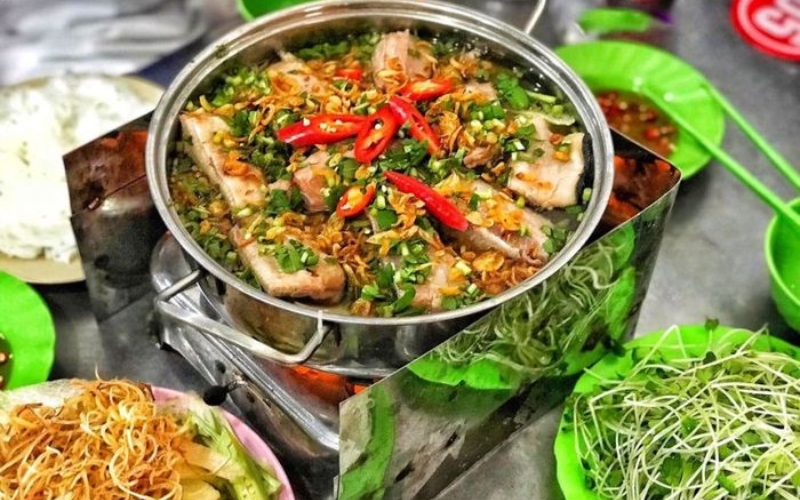 A steaming pot of Vietnamese stingray hot pot with fresh herbs, vegetables, and dipping sauce, served at a seaside restaurant in Vung Tau.