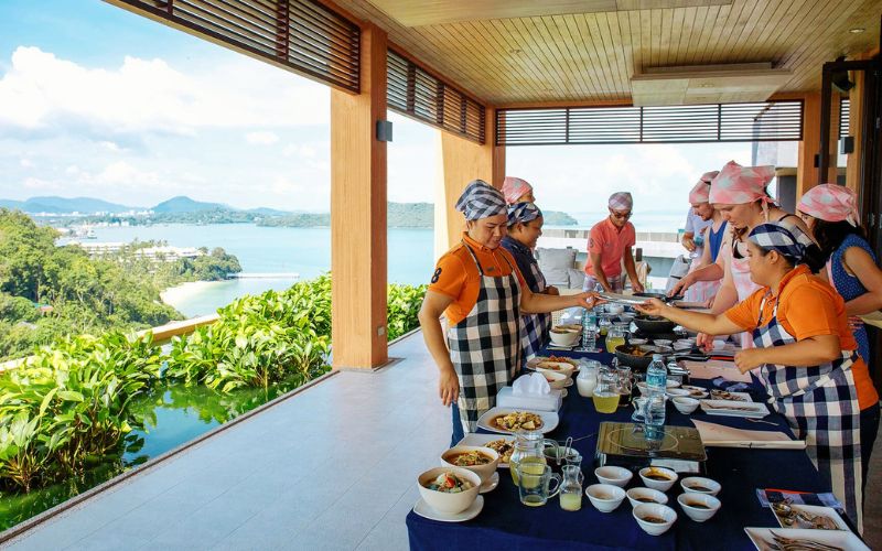 A group of tourists participate in a Thai Cooking Class with a view overlook the pristine beach in Phuket