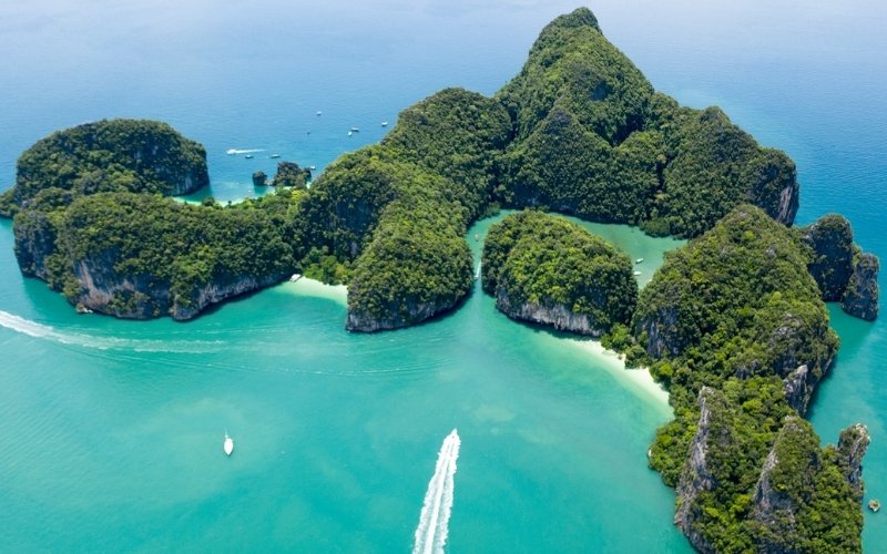 Aerial view of Hong Island in Thailand, featuring lush green limestone formations surrounded by clear turquoise waters and white sandy beaches, with boats cruising around.