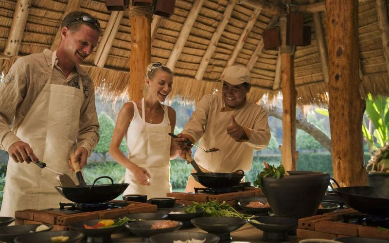Tourists learning Thai cooking with a local chief in an outdoor kitchen setting