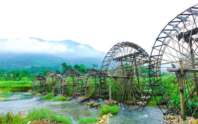 Traditional bamboo waterwheels at Tien Moi Bridge in Pu Luong, set against lush greenery and misty mountain backdrops