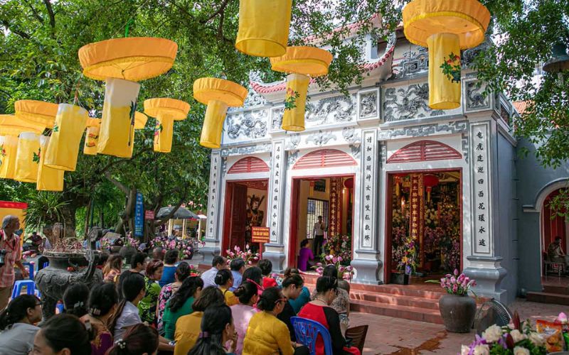 Local people gathered for a ceremony at the Tay Ho Communal House Festival, decorated with yellow hanging lanterns and floral arrangements.
