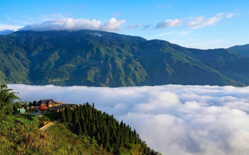 Sea of clouds covering the valleys at Ta Xua, Son La, Vietnam, with green mountain slopes and a clear blue sky in the background