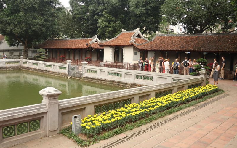 A wide view of the third courtyard featuring the square Well of Heavenly Clarity (Gieng Thien Quang) in the center. Surrounding the water are the famous stone doctoral stelae mounted on the backs of stone tortoises, sheltered under long tiled-roof pavilions on either side.