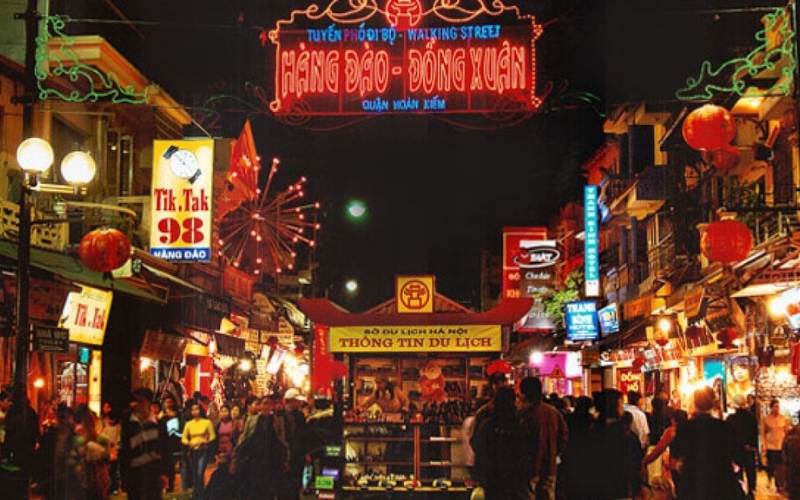 A lively evening scene at Hanoi’s Hang Dao Night Market, with rows of colorful stalls, glowing lanterns, and locals and tourists browsing for souvenirs, clothes, and street snacks.