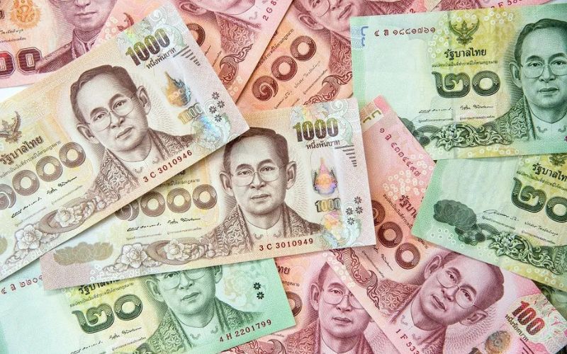 Various denominations of Thai baht banknotes, including 20, 100, 500, and 1000 baht bills, featuring portraits of King Bhumibol Adulyadej
