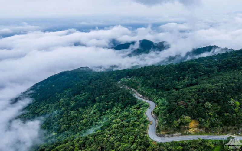 Winding mountain road surrounded by lush green hills and drifting clouds in Tam Dao