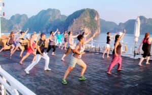 Travelers practicing tai chi on a cruise deck in Ha Long Bay, Vietnam, with limestone karsts in the background at sunrise