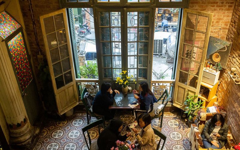 Cozy interior of Loading T Café in Hanoi, featuring vintage French architecture, warm lighting, and large windows overlooking the street