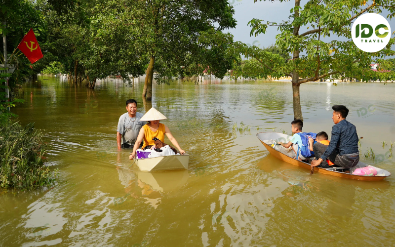 Residents wading and paddling small boats through a flooded village street in Vietnam during typhoon season.