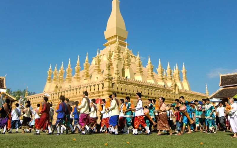 Crowd of people in colorful traditional clothing celebrating at That Luang Festival in front of the golden Pha That Luang stupa in Vientiane, Laos.