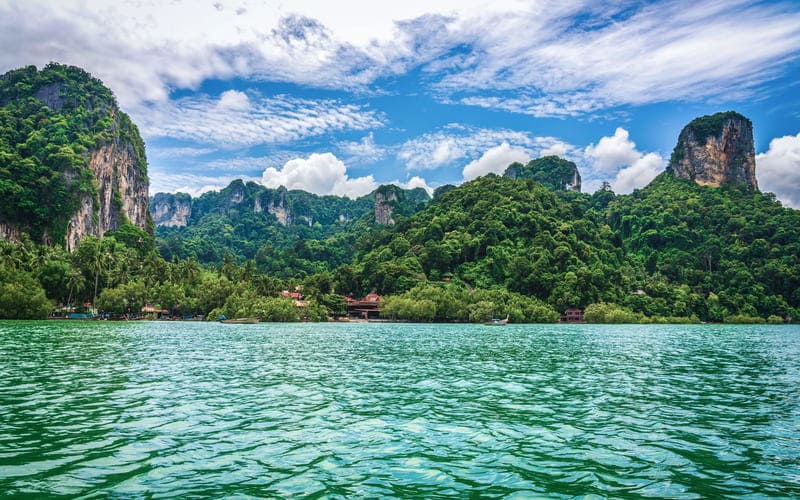 Scenic view of emerald-green water surrounded by lush tropical mountains and blue sky in southern Thailand after the rain.