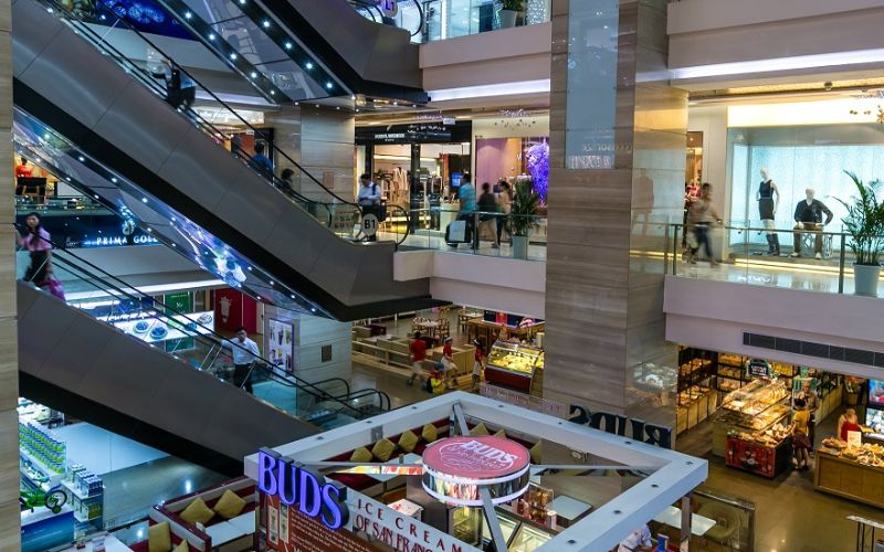 The modern interior of Vincom Center Dong Khoi, featuring multiple levels of high-end retail stores, sleek glass railings, and long escalators connecting the bright, white shopping floors.