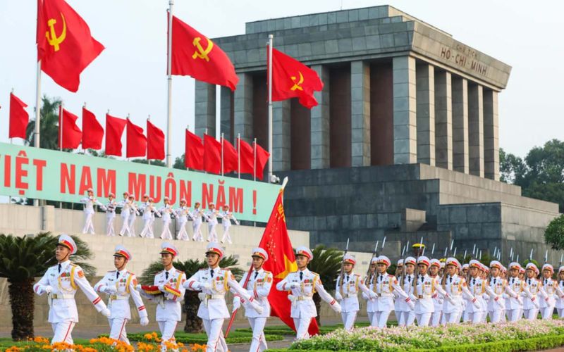Vietnamese soldiers in white ceremonial uniforms marching in a parade in front of the Ho Chi Minh Mausoleum during Vietnam National Day Celebrations.