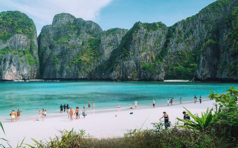 Tourists relaxing on white sand beach at Maya Bay, Koh Phi Phi, surrounded by limestone cliffs and turquoise water