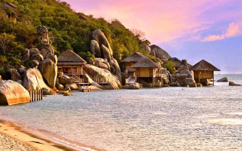 Beautiful sunset over Van Phong Bay with rocky coast, calm sea, and wooden huts by the beach in Khanh Hoa