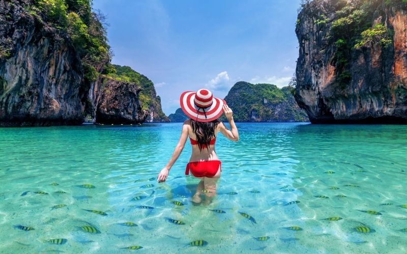 Woman in red bikini soaking in crystal-clear turquoise waters with limestone cliffs in Phuket, Thailand