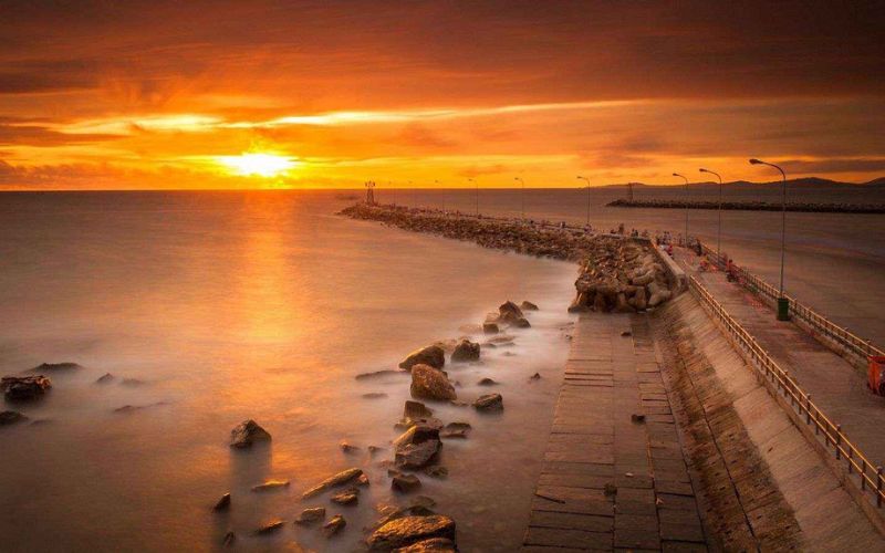 Golden sun sinking into the horizon over Phu Quoc’s calm sea, with palm trees swaying in the evening breeze.