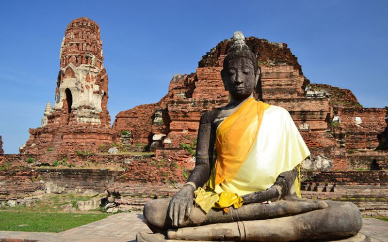 Ancient Buddha statue at Wat Phra Mahathat in Ayutthaya, Thailand, with historic temple ruins in the background