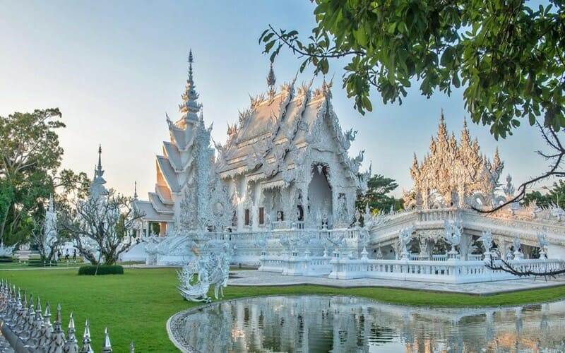 The White Temple (Wat Rong Khun) in Chiang Rai, Thailand, glowing under the soft morning light with its intricate white carvings reflected in a small pond.