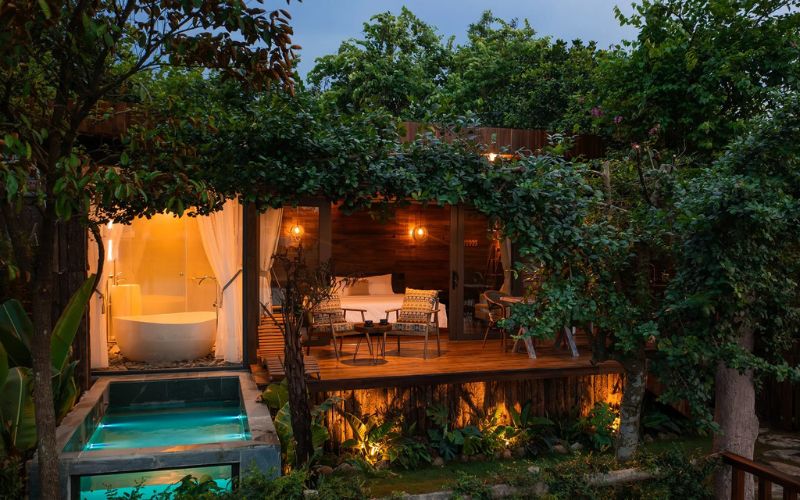 Cozy wooden cabin at Xuan Son Lakeview Homestay in Phu Tho, Vietnam, with warm lighting, surrounded by lush trees and a small outdoor pool