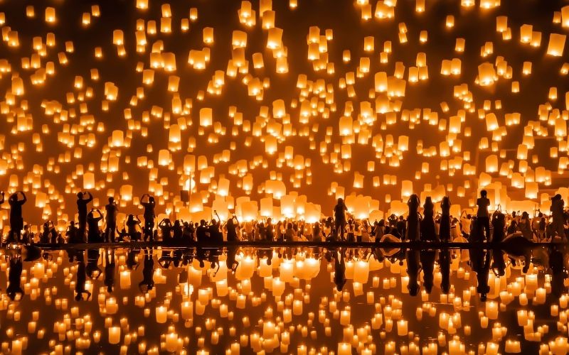 Sky lanterns fill the night sky during the Yi Peng Festival in Chiang Mai, Thailand, with reflections glowing on the water